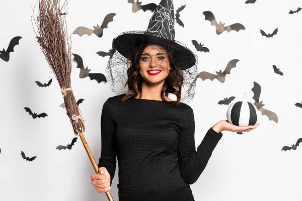 Беременная женщина в шляпе ведьмы держит метлу и тыкву в Хэллоуин — стоковое фото