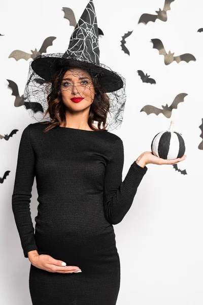 Беременная женщина в шляпе ведьмы держит тыкву в Хэллоуин — стоковое фото