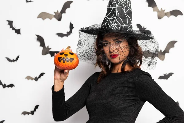 Jolie femme en chapeau de sorcière tenant citrouille à Halloween — Photo de stock