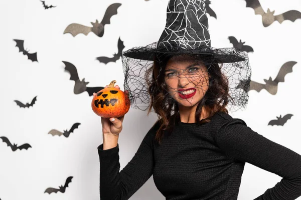 Angry woman in witch hat holding pumpkin in Halloween — Stock Photo