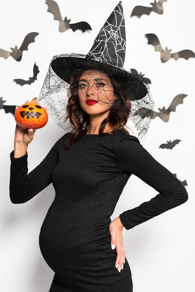 Беременная женщина в шляпе ведьмы держит тыкву в Хэллоуин — стоковое фото