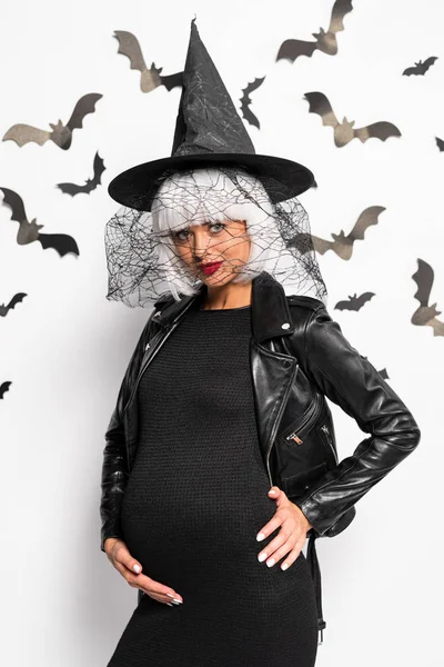 Femme enceinte en chapeau de sorcière et perruque regardant la caméra à Halloween — Photo de stock