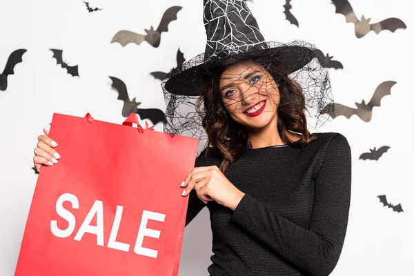 Улыбающаяся женщина в шляпе ведьмы держит сумку с надписью продажи в Хэллоуин — стоковое фото