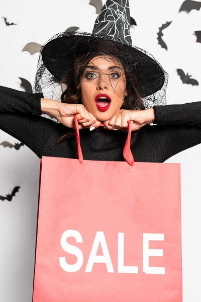 Шокированная женщина в шляпе ведьмы держит сумку с надписью продажи в Хэллоуин — стоковое фото