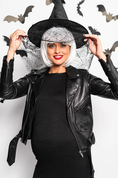 Femme enceinte en chapeau de sorcière et perruque souriant à Halloween — Photo de stock