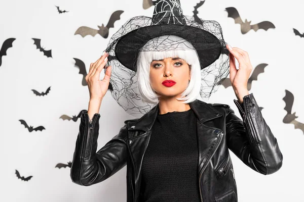 Atractiva mujer en sombrero de bruja y peluca mirando a la cámara en Halloween - foto de stock