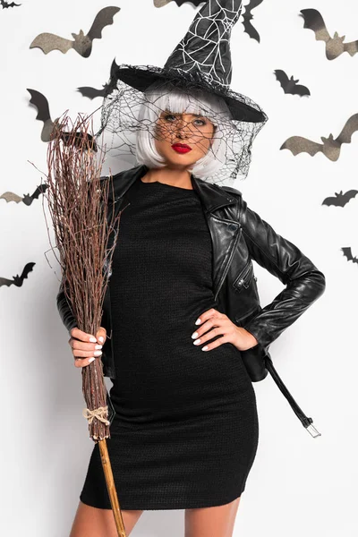 Atractiva mujer en sombrero de bruja y peluca con escoba en Halloween - foto de stock