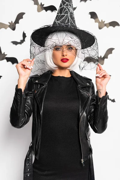 Mulher atraente em chapéu de bruxa e peruca olhando para a câmera no Halloween — Fotografia de Stock