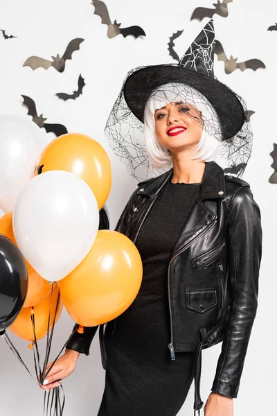 Mulher sorridente em chapéu de bruxa e peruca segurando balões no Halloween — Fotografia de Stock
