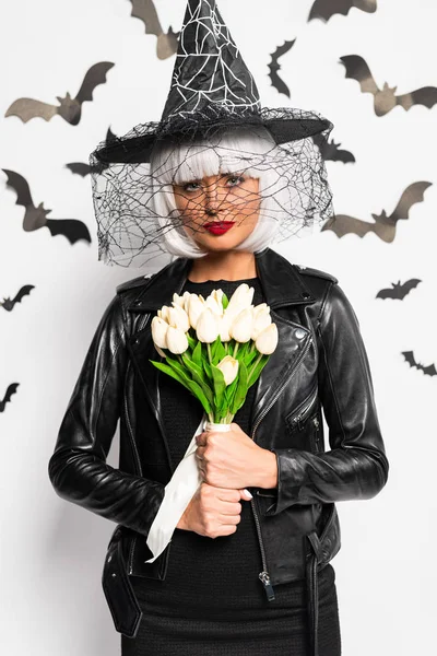 Mulher atraente em chapéu de bruxa e peruca segurando buquê no Halloween — Fotografia de Stock