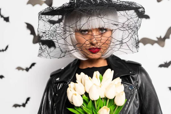 Mulher atraente em chapéu de bruxa e peruca segurando buquê no Halloween — Fotografia de Stock