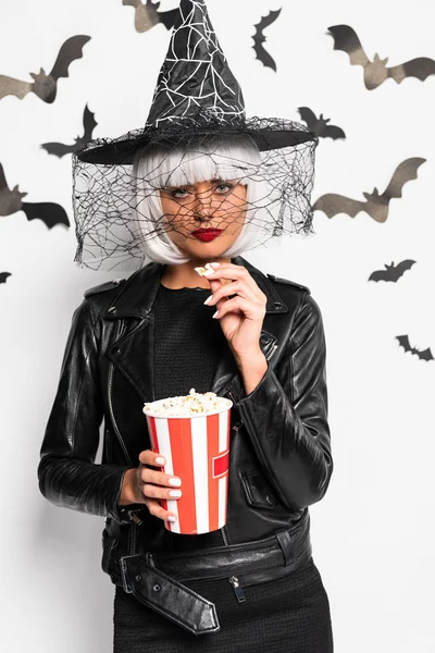 Atractiva mujer en sombrero de bruja y peluca sosteniendo palomitas de maíz en Halloween - foto de stock