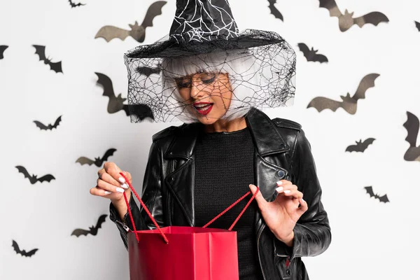 Mujer sorprendida en sombrero de bruja y peluca sosteniendo bolsa de compras en Halloween - foto de stock