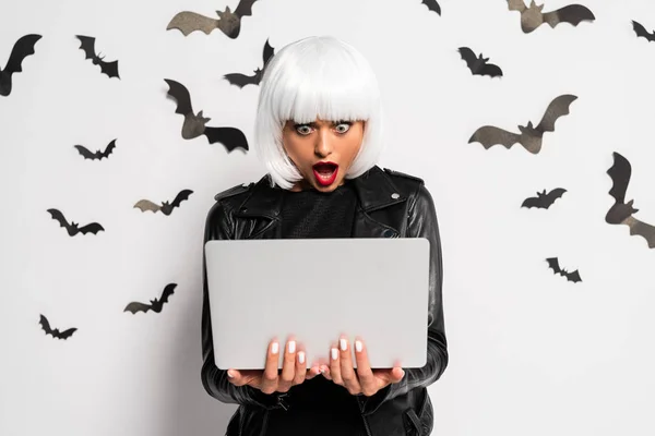Mujer conmocionada en peluca blanca sosteniendo portátil en Halloween - foto de stock