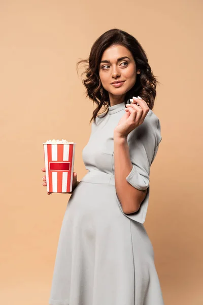 Pregnant woman in grey dress holding popcorn on beige background — Stock Photo