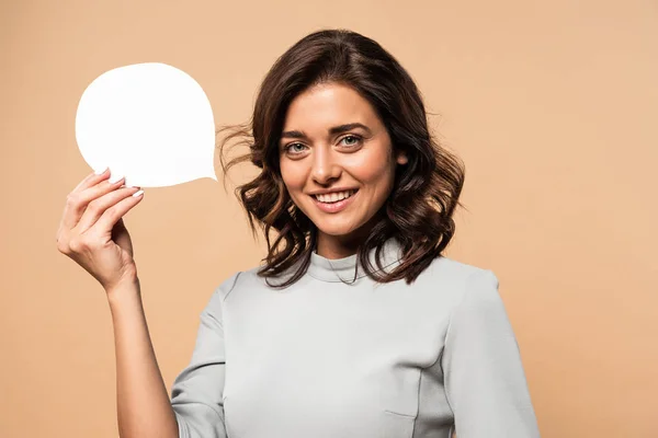 Mulher sorridente em vestido cinza segurando bolha discurso isolado no bege — Fotografia de Stock