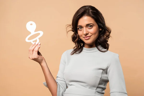 Pregnant woman in grey dress holding paper pacifier on beige background — Stock Photo