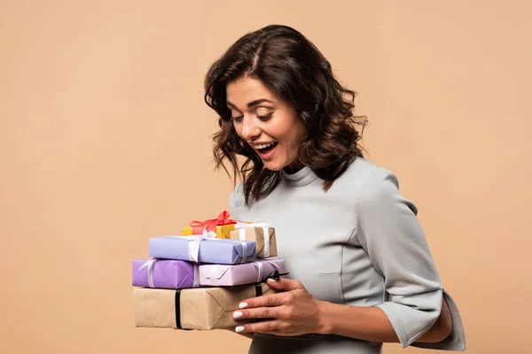 Mujer sonriente en vestido gris sosteniendo regalos sobre fondo beige - foto de stock