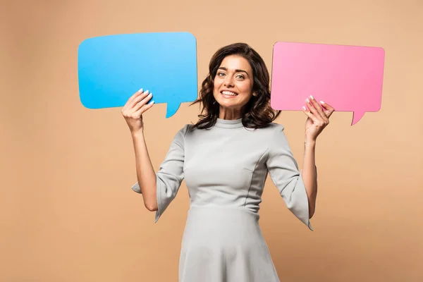 Pregnant woman in grey dress holding speech bubbles on beige background — Stock Photo