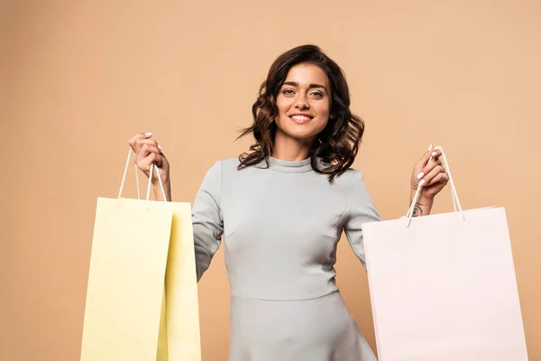 Pregnant woman in grey dress smiling and holding shopping bags on beige background — Stock Photo