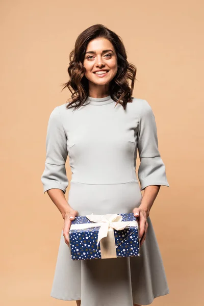 Femme enceinte en robe grise souriante et tenant cadeau sur fond beige — Photo de stock