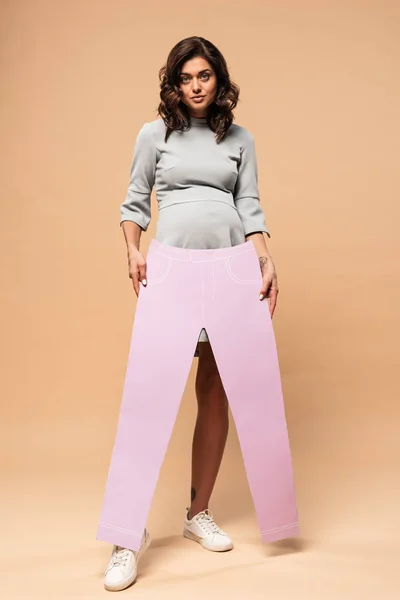 Pregnant woman in grey dress paper trousers on beige background — Stock Photo