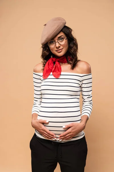 Pregnant french woman in beret looking at camera on beige background — Stock Photo
