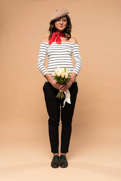 Pregnant french woman in beret holding bouquet on beige background — Stock Photo