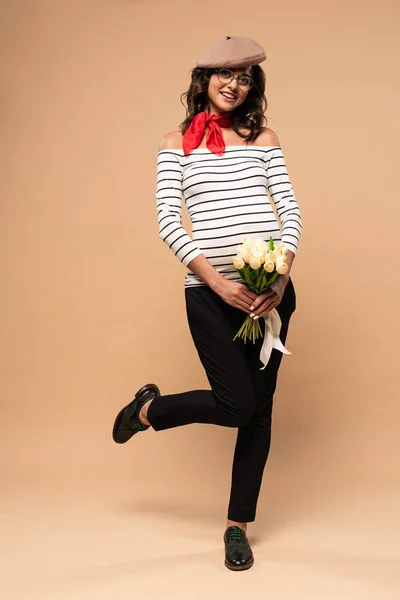 Pregnant french woman in beret holding bouquet on beige background — Stock Photo