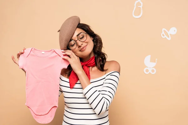 Pregnant french woman with closed eyes in beret holding overalls isolated on beige — Stock Photo