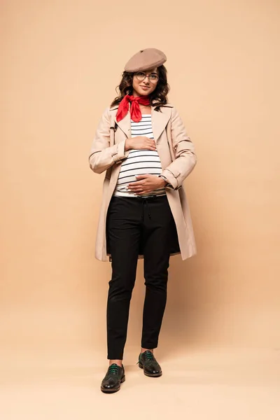 Беременная француженка в пальто смотрит в камеру на бежевом фоне — стоковое фото