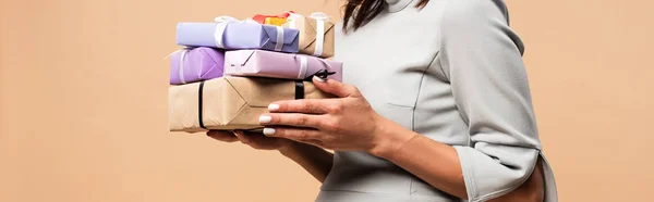 Panoramic shot of pregnant woman in grey dress holding gifts isolated on beige — Stock Photo