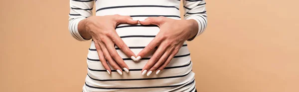 Plano panorámico de la mujer embarazada mostrando el signo del corazón aislado en beige - foto de stock