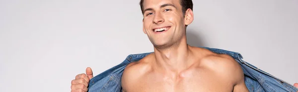 Panoramic shot of cheerful man taking off denim shirt on white — Stock Photo