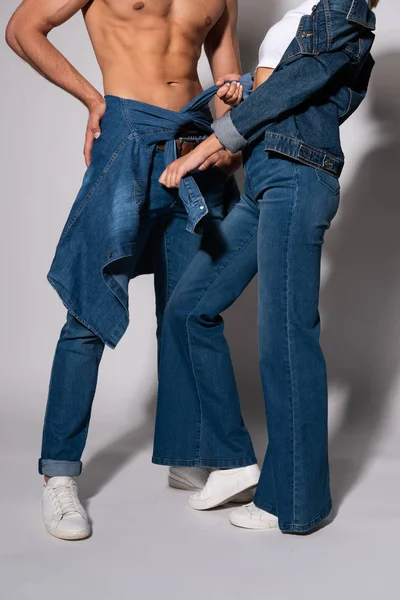 Corte vista de mulher tocando camisa jeans de homem muscular em pé no branco — Fotografia de Stock