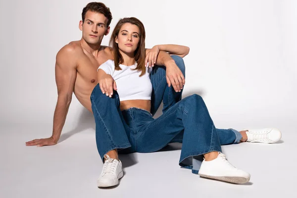 Pretty woman in denim jeans sitting with sexy man on white — Stock Photo