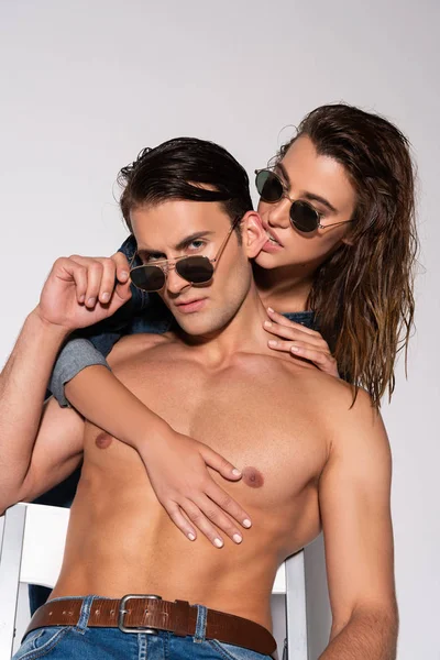 Apasionada chica mordiendo oreja de moda y musculoso hombre en gafas de sol en blanco - foto de stock