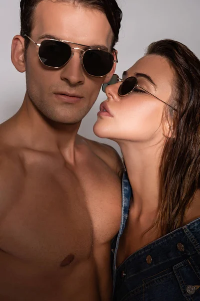Donna attraente in occhiali da sole e giacca di jeans vicino all'uomo elegante e muscoloso sul bianco — Foto stock