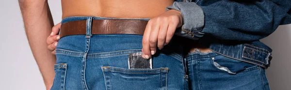 Tiro panorâmico de menina colocando preservativo no bolso do homem em jeans no branco — Fotografia de Stock