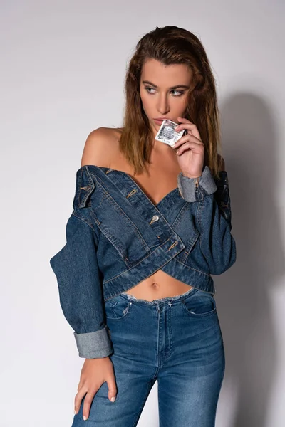 Sexy girl in denim jeans standing and holding condom on white — Stock Photo