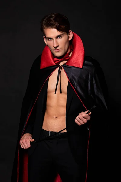 Hombre en vampiro halloween traje celebración azotes látigo aislado en negro - foto de stock