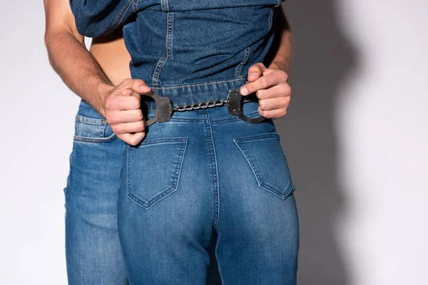 Vista ritagliata dell'uomo che tiene le manette vicino alla ragazza in jeans su bianco — Foto stock