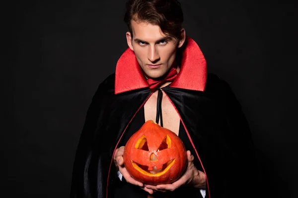 Handsome man holding halloween pumpkin isolated on black — Stock Photo