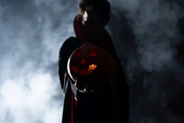 Selective focus of man holding pumpkin on black with smoke — Stock Photo