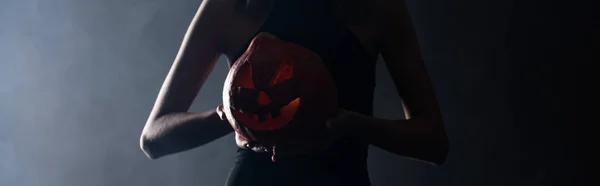 Panoramic shot of woman holding spooky pumpkin on black with smoke — Stock Photo