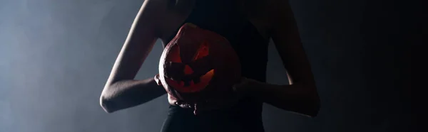 Plano panorámico de mujer sosteniendo espeluznante calabaza en negro con humo - foto de stock