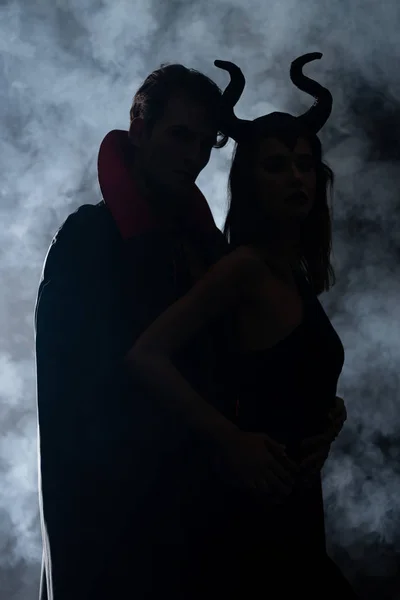 Silhouette d'homme et de femme en costumes d'Halloween sur noir avec de la fumée — Photo de stock