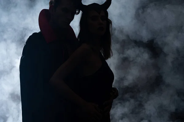 Silueta del hombre y la mujer en trajes de Halloween de pie en negro con humo - foto de stock