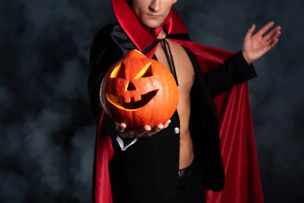 Vista recortada del hombre sosteniendo la calabaza de halloween y el gesto en negro con humo - foto de stock