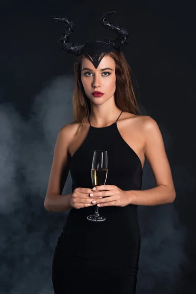 Attraente donna con le corna in possesso di bicchiere di champagne su nero con fumo — Foto stock